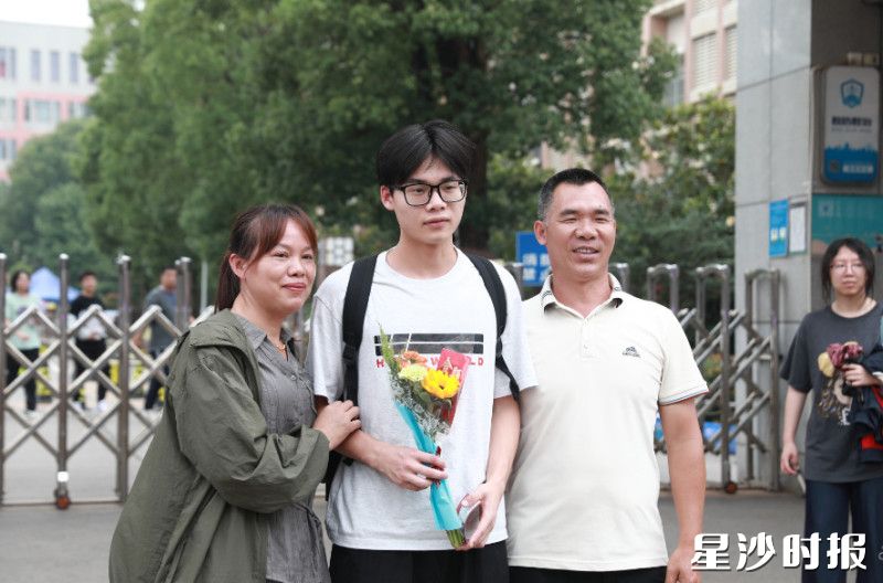 在长沙市明达高级中学考点，考生手捧鲜花，与家长合影。