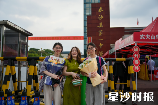 长沙县一中考点，一位年轻的妈妈手捧两束鲜艳的向日葵，踮着脚尖，在人群中急切地张望着。当看到双胞胎女儿走出考场时，她立刻扬起灿烂的笑容，挥舞着花束迎了上去。拍照时，害羞的父亲躲在一旁，用满含爱意的目光注视着妻子和女儿。黄宇 摄