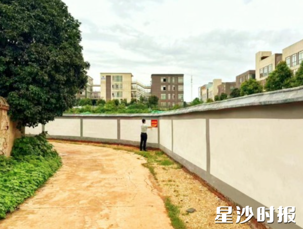 网格员在围墙上张贴禁止圈地种菜的宣传标语。
