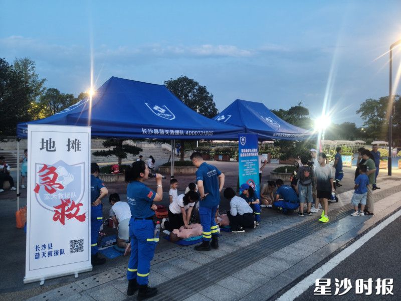 志愿者正手持话筒，热情地向过往市民介绍“急救地摊”。