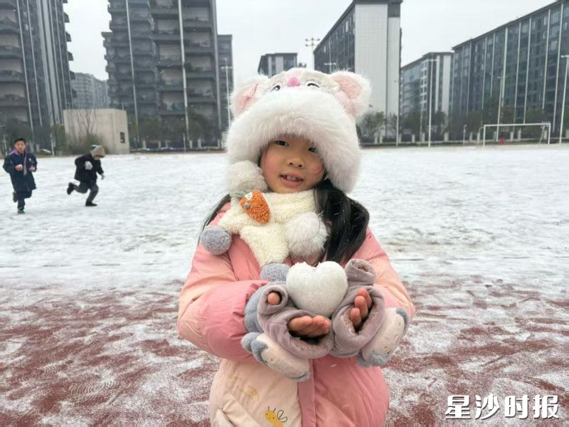 在长沙市育英会展小学，小女孩捧着一颗雪团捏成的小心心，笑容像阳光一样暖化了冬日的寒意。