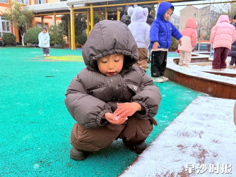 在㮾梨街道中心幼儿园，小朋友捧着一小团雪仔细端详。身后小伙伴们的身影在飘雪的操场里晃着，是童年最纯粹的冬日模样。