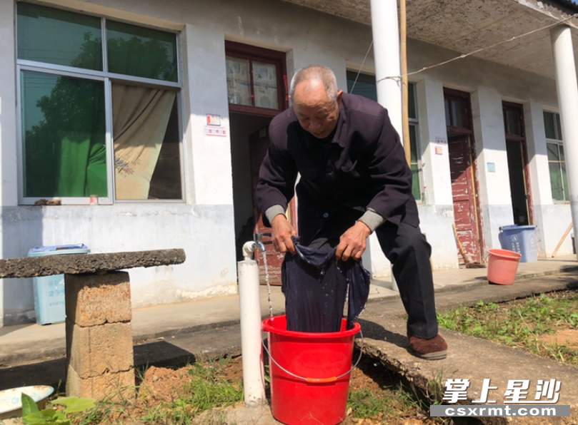 春华镇武塘村秀才湾组分散供养特困人员龙培恺在房前打开水龙头洗衣服。