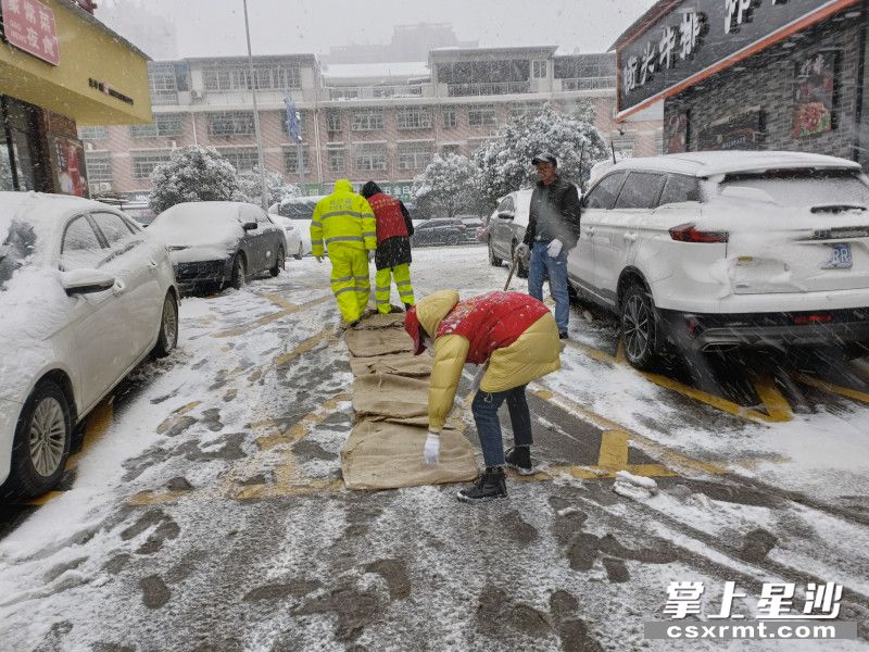 图为长沙县㮾梨街道志愿者正清扫道路积雪，并于湿滑路段铺设麻袋。供图