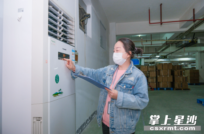 张露在仓库空调旁记录温度调控。章帝 摄