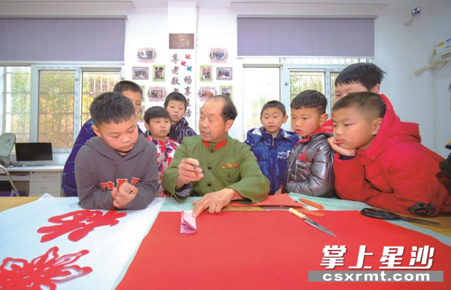 在长沙县新时代文明实践所里，手艺人在向周围孩童展示剪纸工艺。章帝 摄