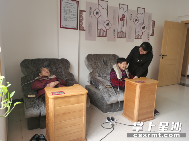 在社区居家养老服务中心，杨密（右）在帮助前来理疗的老人调试肩带按摩器。