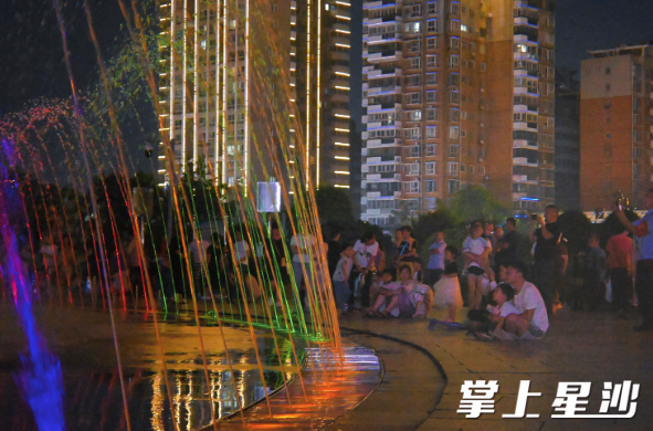 市民们或坐或站在音乐喷泉周围，享受视听盛宴。