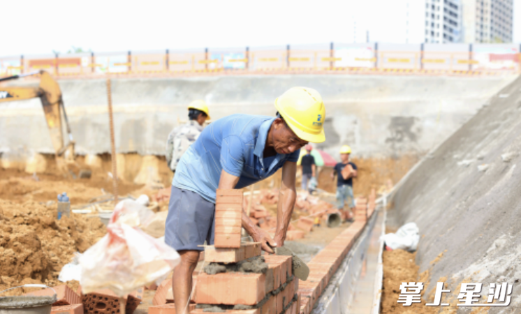 在基坑与边坡衔接区域，伍满意与十多名工人忙着搬砖砌墙，虽然酷暑难耐，但医院早一天建好，就能让更多老百姓得实惠，他和工友们干劲十足。 