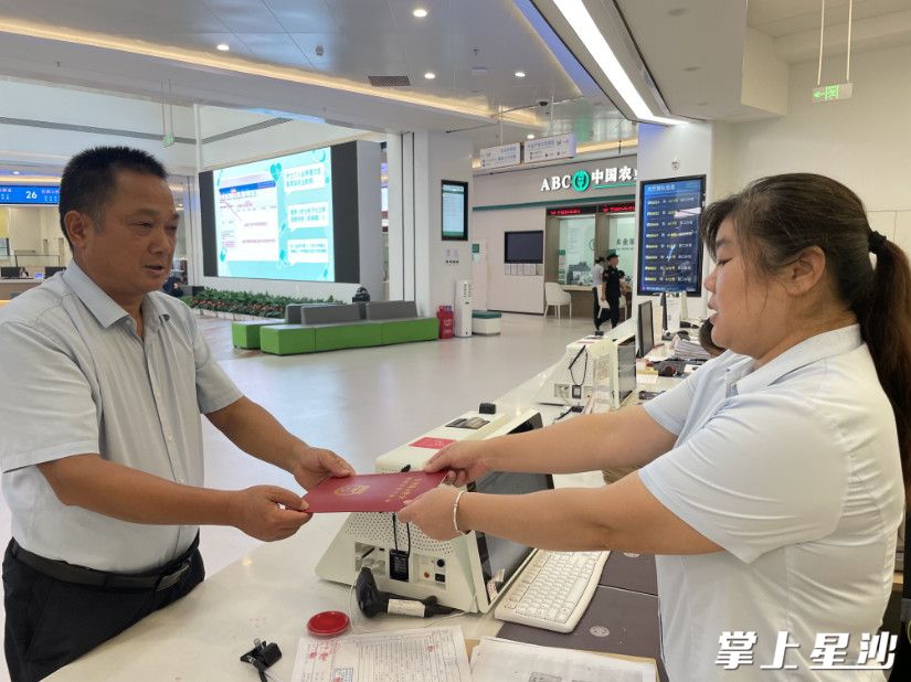 罗科明（左）在不动产登记中心窗口领取到了农村集体建设用地不动产权证书。县自资局供图