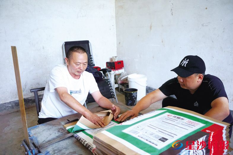 湖南兴中迪包装有限公司相关负责人周希旦(右)手把手教李大哥(左)折纸袋。 吴婉沁 摄