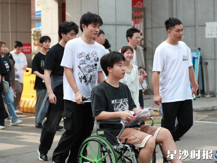 在黄兴镇长沙市明达中学考点，一位受伤考生坐着轮椅，被同学推着一起走进考场。李杰 摄
